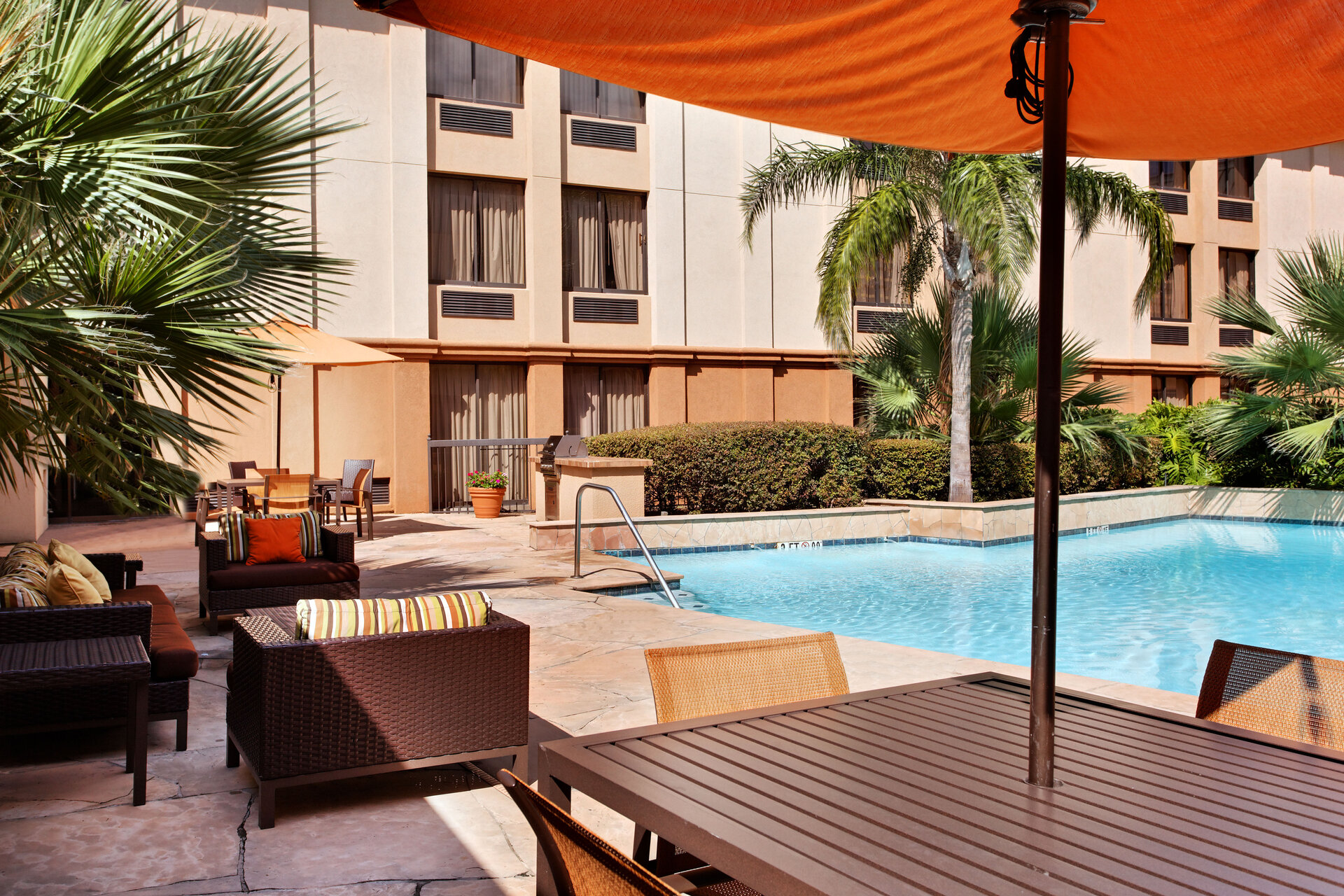 A poolside area with furniture, umbrella, and palm trees in front of a building